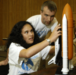 A blind girl explores a model of a space shuttle as a facilitator looks on.